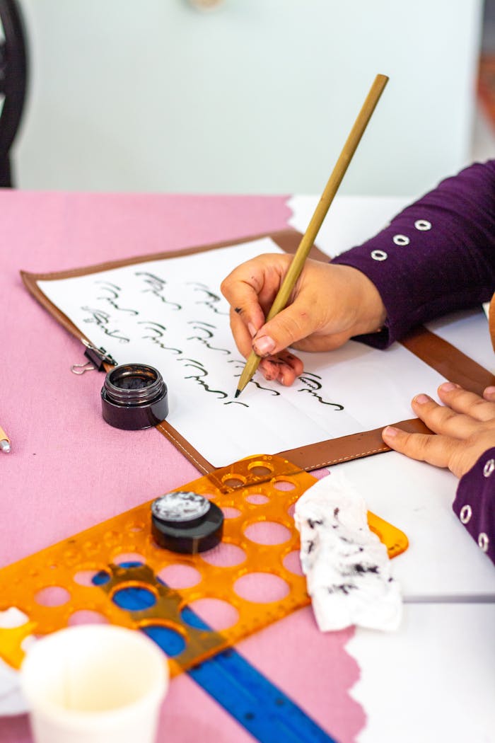 A person practicing calligraphy with ink and pen on paper, close-up view.