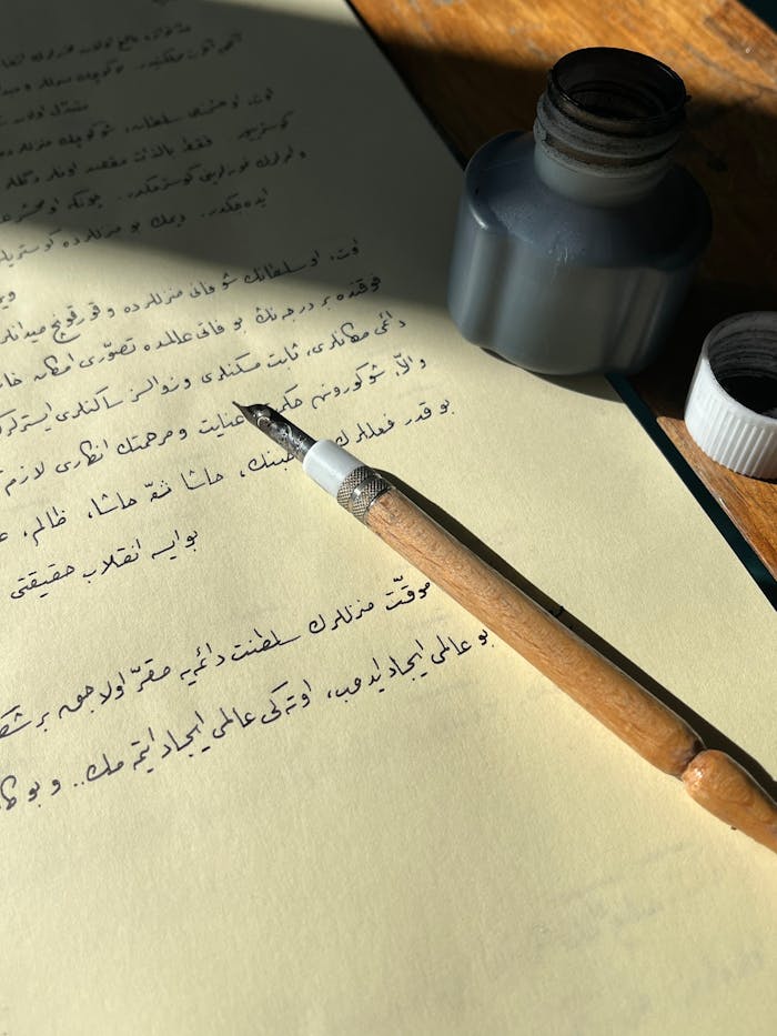 A vintage calligraphy pen rests on Arabic script paper beside an ink bottle.