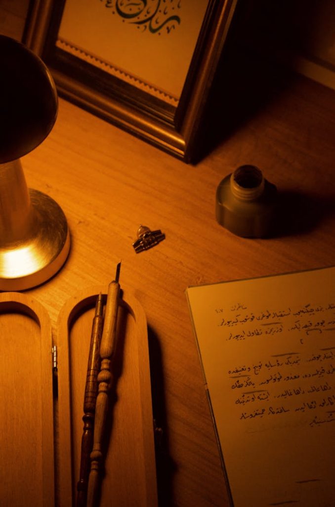 Warmly lit artistic desk featuring calligraphy, ink pen, and ink bottle creating a cozy ambiance.