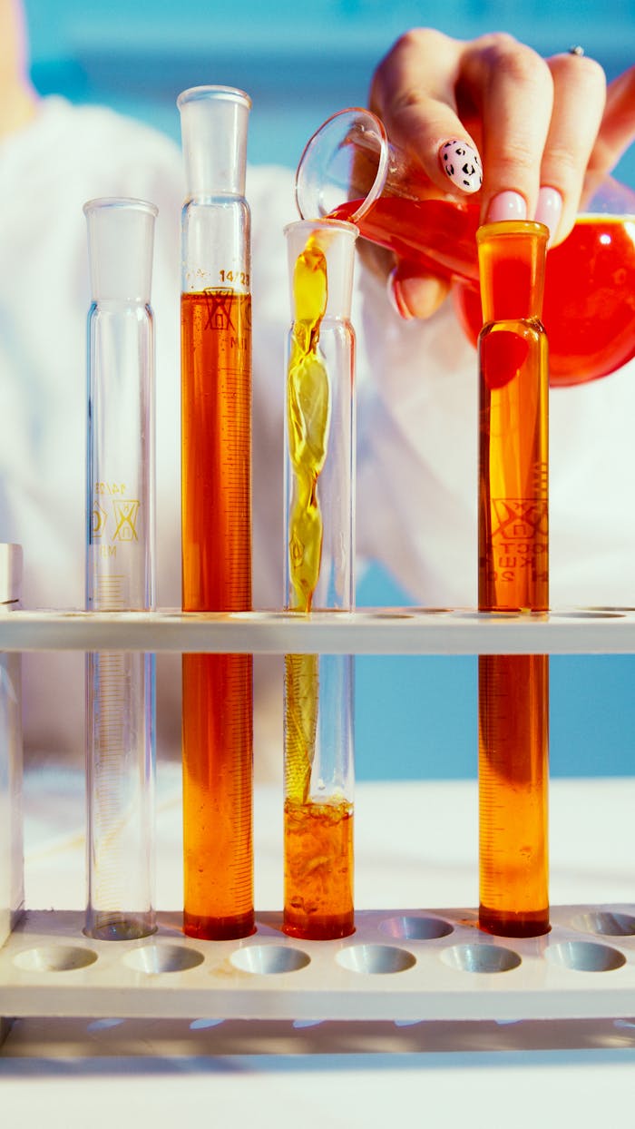 Close-up of a lab technician pouring orange liquid into test tubes in a laboratory setting.