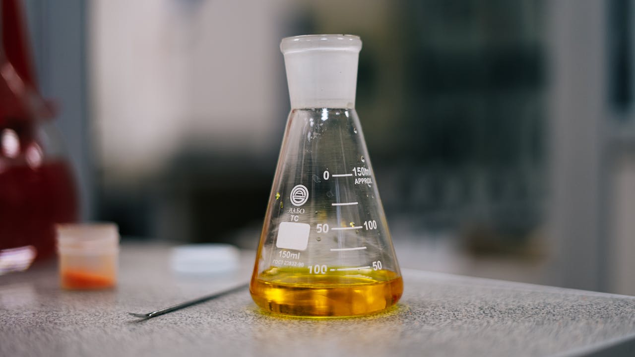 Close-up of an Erlenmeyer flask with yellow liquid in a laboratory setting.